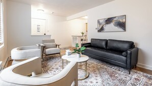 A modern living room with a black leather sofa, white armchairs, a coffee table, and a patterned rug.
