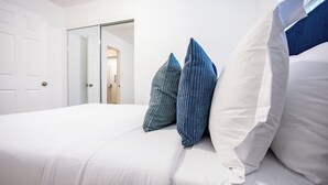 A neatly made bed with white and blue pillows, a white door, and a glass door leading to another room.
