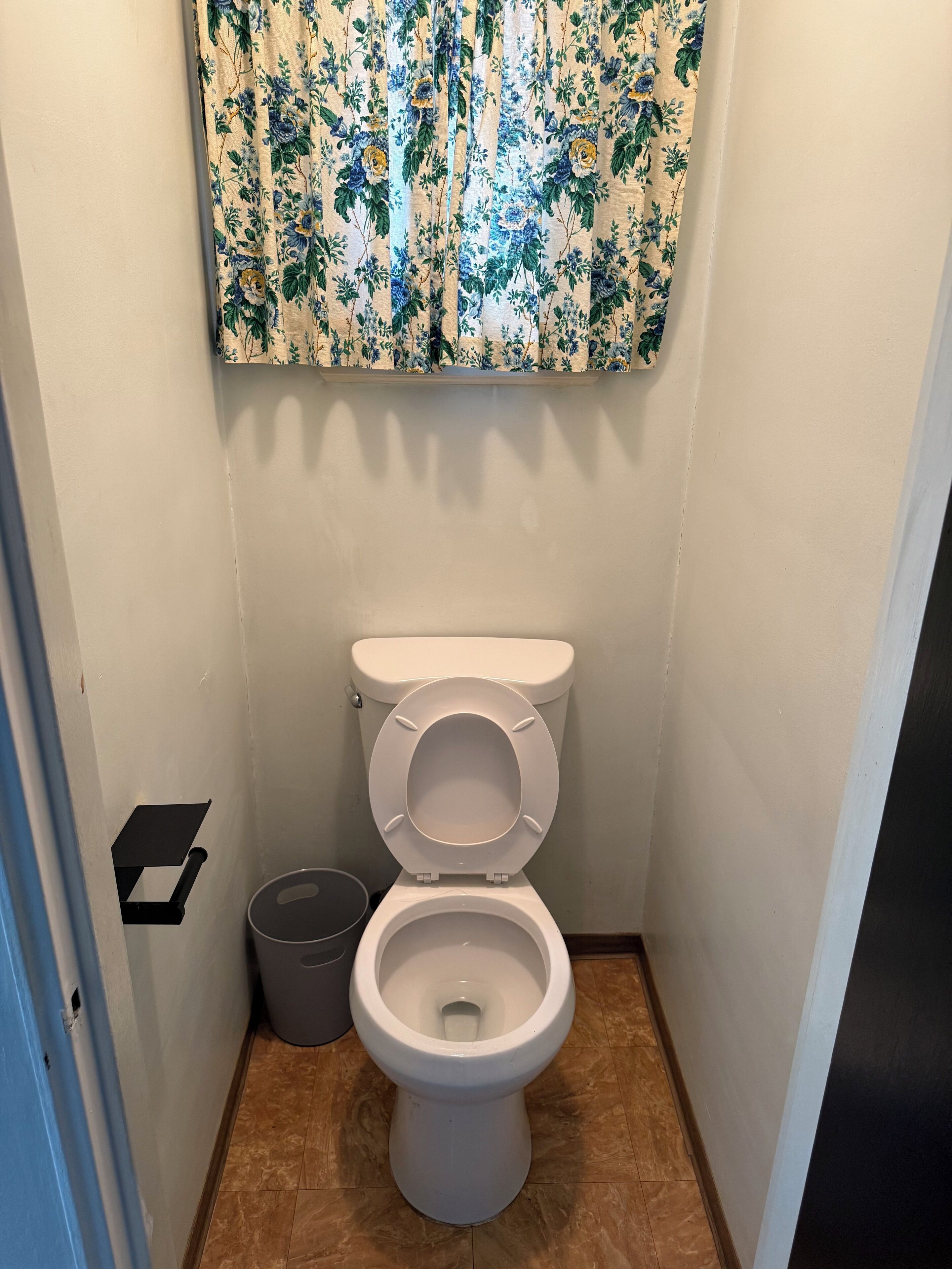 A small bathroom with a toilet, a trash bin, and a wall-mounted shelf.