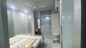 Een slaapkamer met een bed, een plafondventilator, een raam en een klein tafeltje.