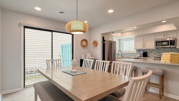 A modern kitchen with white cabinets, stainless steel appliances, and a dining area with a wooden table and white chairs. - Updated 3BR Beach House • 3 Blocks to Ocean • Fenced Yard • Grill (North Myrtle Beach)