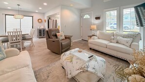 A spacious living room with a ceiling fan, a dining area with a table and chairs, a sofa, and a coffee table with a tray. - Updated 3BR Beach House • 3 Blocks to Ocean • Fenced Yard • Grill (North Myrtle Beach)