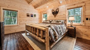 A wooden cabin bedroom with a bed, two windows, a heart-shaped wall decoration, and a dresser. - New Rangeley Mountain Home with Snowmobile Trail Access | Sleeps 9 (Rangeley)