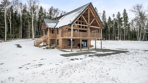 A log cabin with a metal roof, wooden deck, and a staircase leading to the entrance. - New Rangeley Mountain Home with Snowmobile Trail Access | Sleeps 9 (Rangeley)