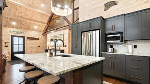 A modern kitchen with a large island, dark cabinets, and a rustic wooden ceiling. - New Rangeley Mountain Home with Snowmobile Trail Access | Sleeps 9 (Rangeley)