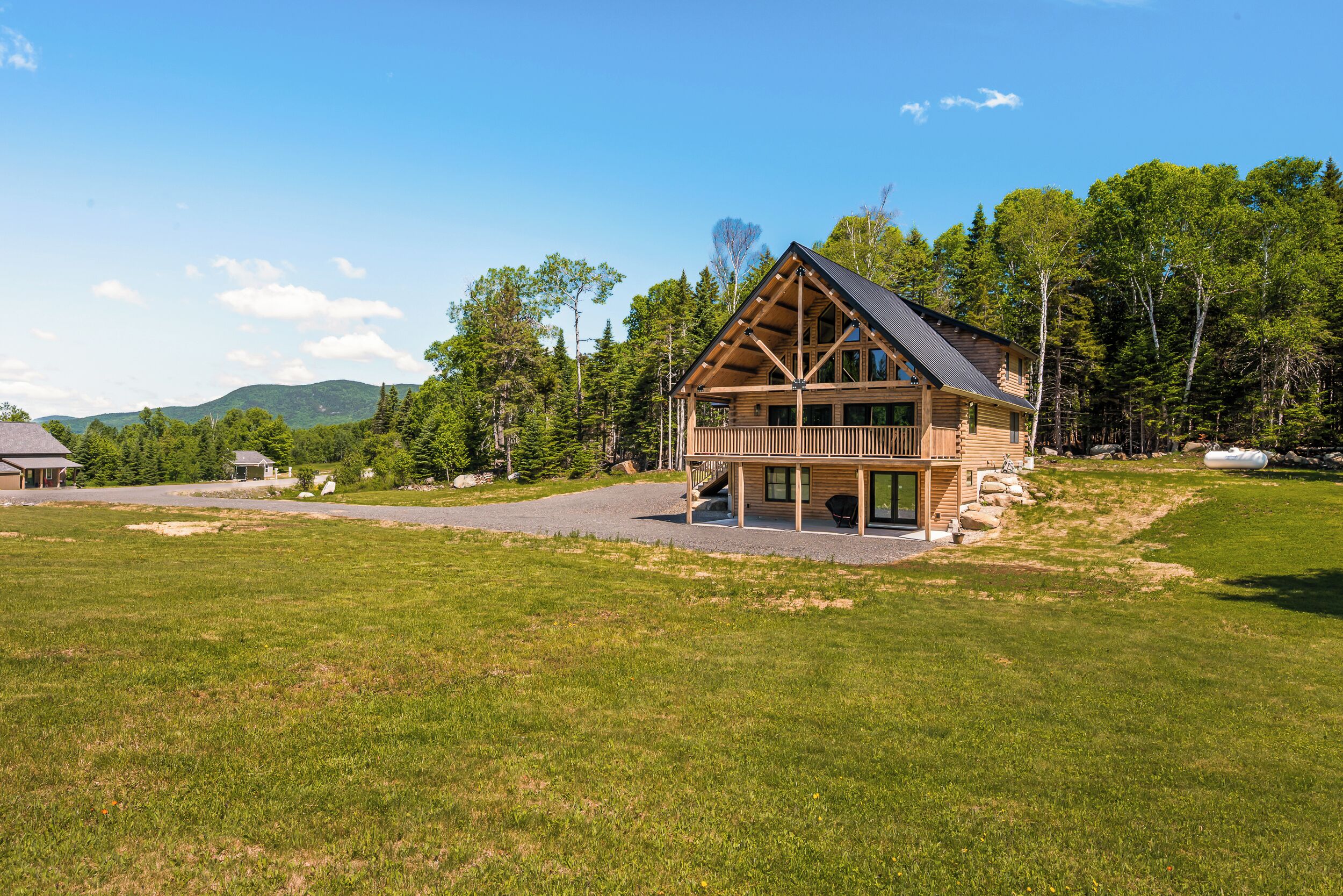 A log cabin with a deck, surrounded by a grassy field and trees.