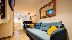 Een woonkamer met een bank, een eettafel en een aan de muur bevestigde televisie.