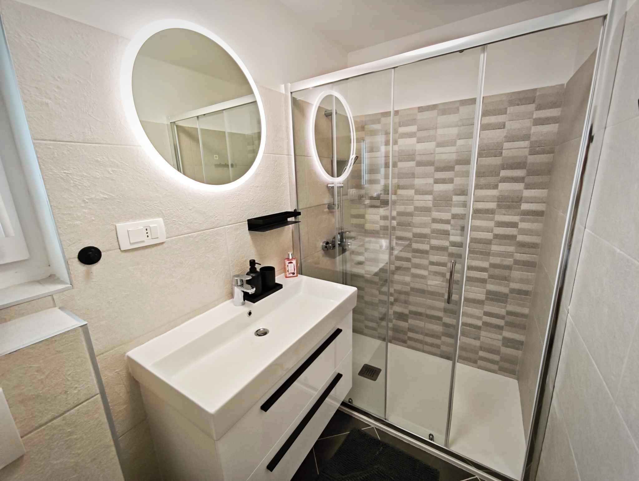 Un bany modern amb un mànec blanc, dos miralls rodons i una cabina de dutxa de vidre.