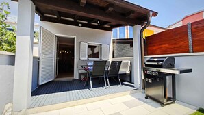 Een terras buiten met een barbecue, een zithoek en een deur naar de binnenruimte.