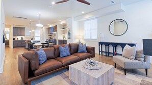 A spacious living room with a brown leather sofa, a grey armchair, a coffee table, and a ceiling fan. - 5 Points East Nashville Luxury | 2 King Suites, Wet Bar & Dual Decks | Sleeps 12 (Nashville)