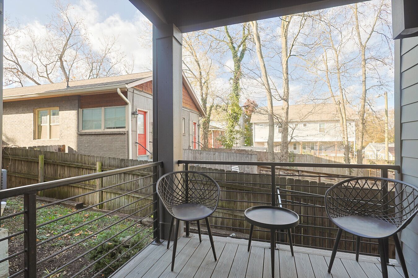 Un espace extérieur abrité, doté d’une terrasse en bois, de deux chaises en métal et offrant une vue sur les maisons voisines.