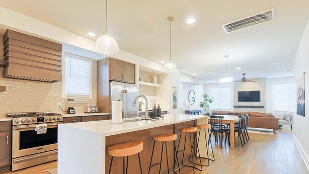 A modern kitchen with a central island, bar stools, and a dining area with a sofa and TV. - 5 Points East Nashville Luxury | 2 King Suites, Wet Bar & Dual Decks | Sleeps 12 (Nashville)