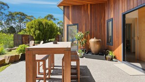 A modern wooden exterior with a patio table and chairs, potted plants, and a large vase. - Tranquility Base - 1 Bedroom Unit - Beachside (Coningham)