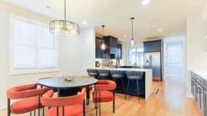 A modern kitchen with a central island, bar stools, and a dining table with chairs.