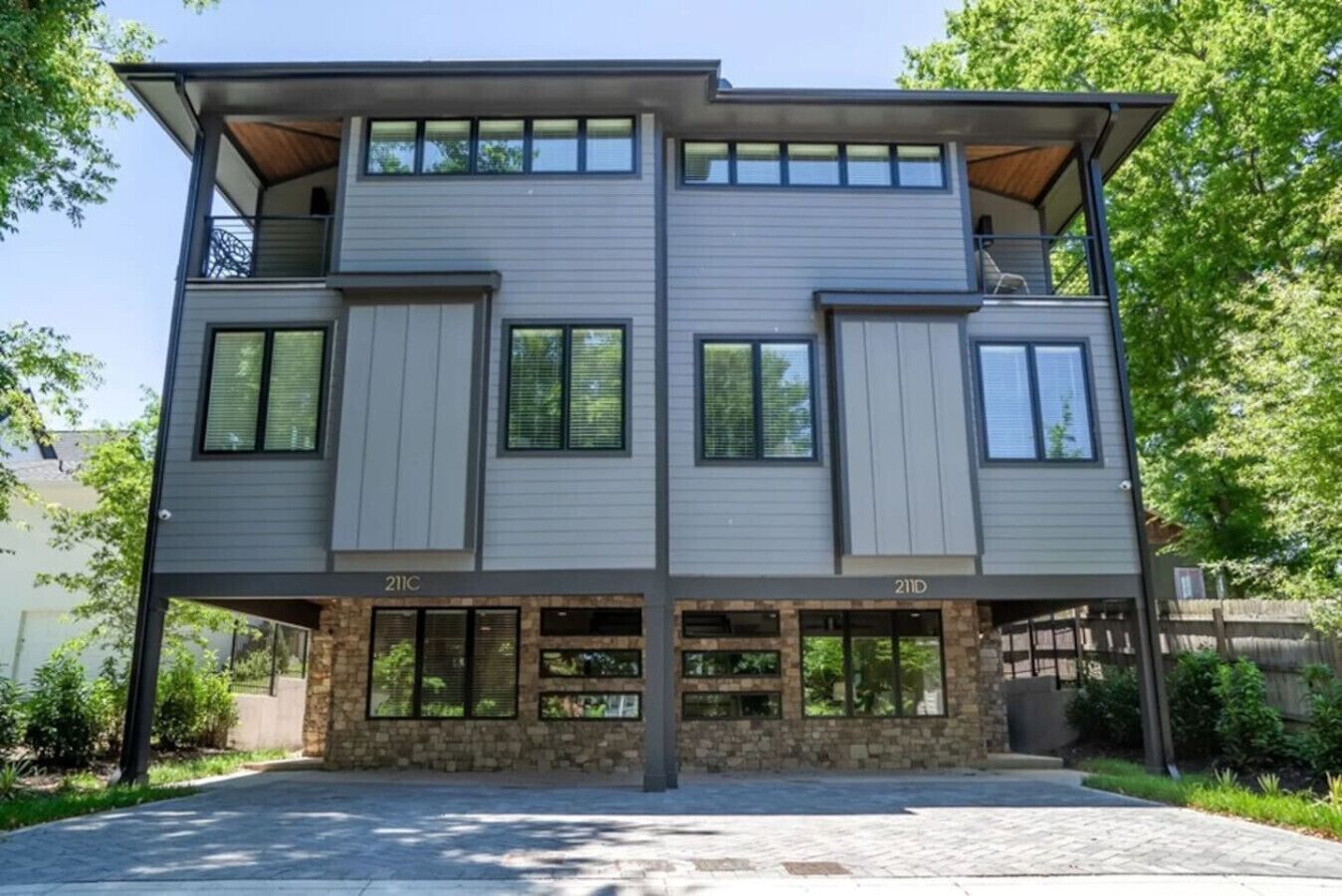 A modern two-story house with a stone foundation, multiple windows, and a balcony on the upper floor.