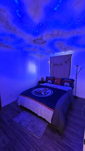 Une chambre à coucher avec un lit aux couleurs des Oilers d’Edmonton, un plafond décoré de motifs étoilés et une lampe sur pied.