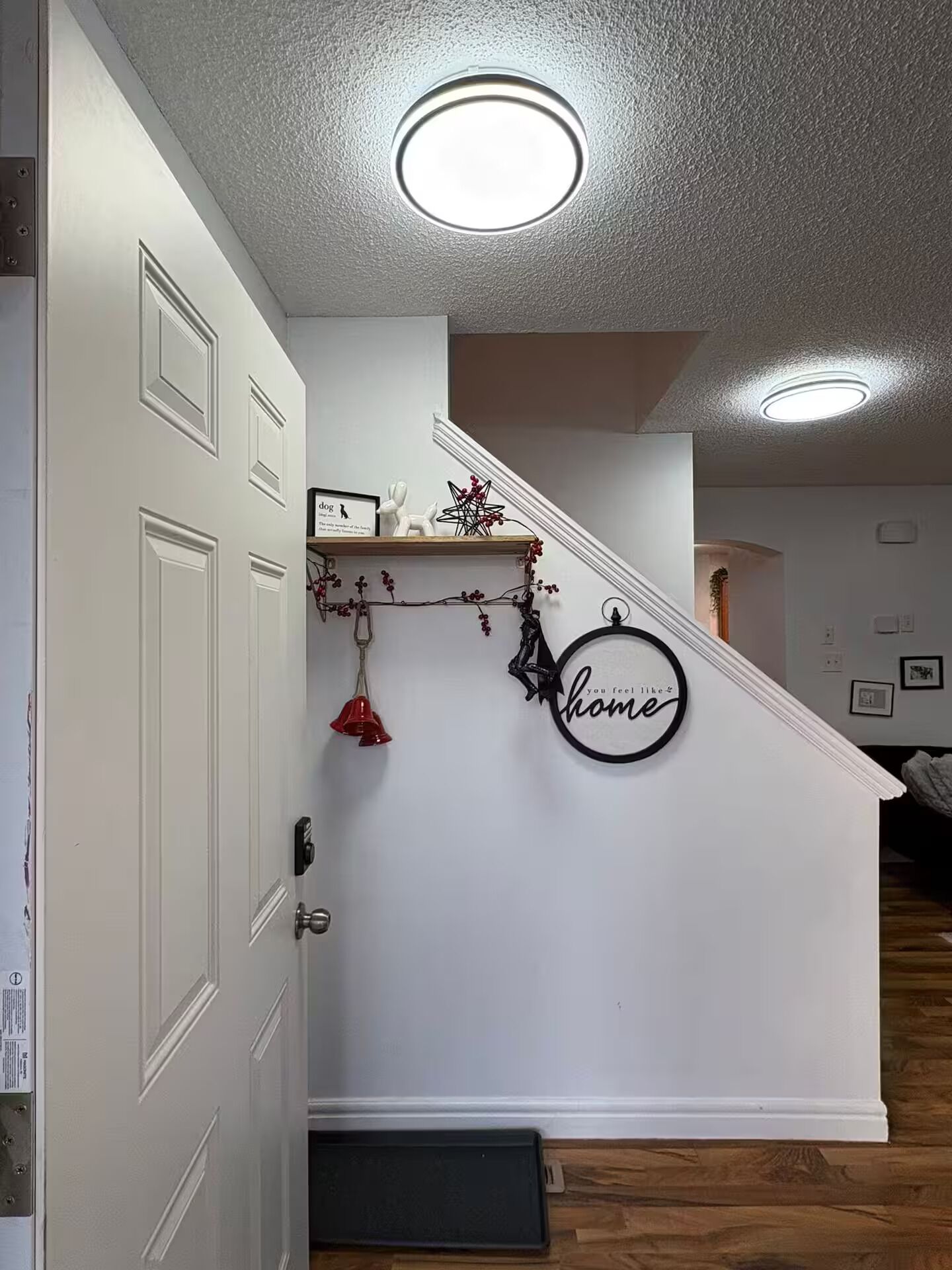 A staircase with a white wall, a small shelf with decorative items, and a circular sign with the word "home".