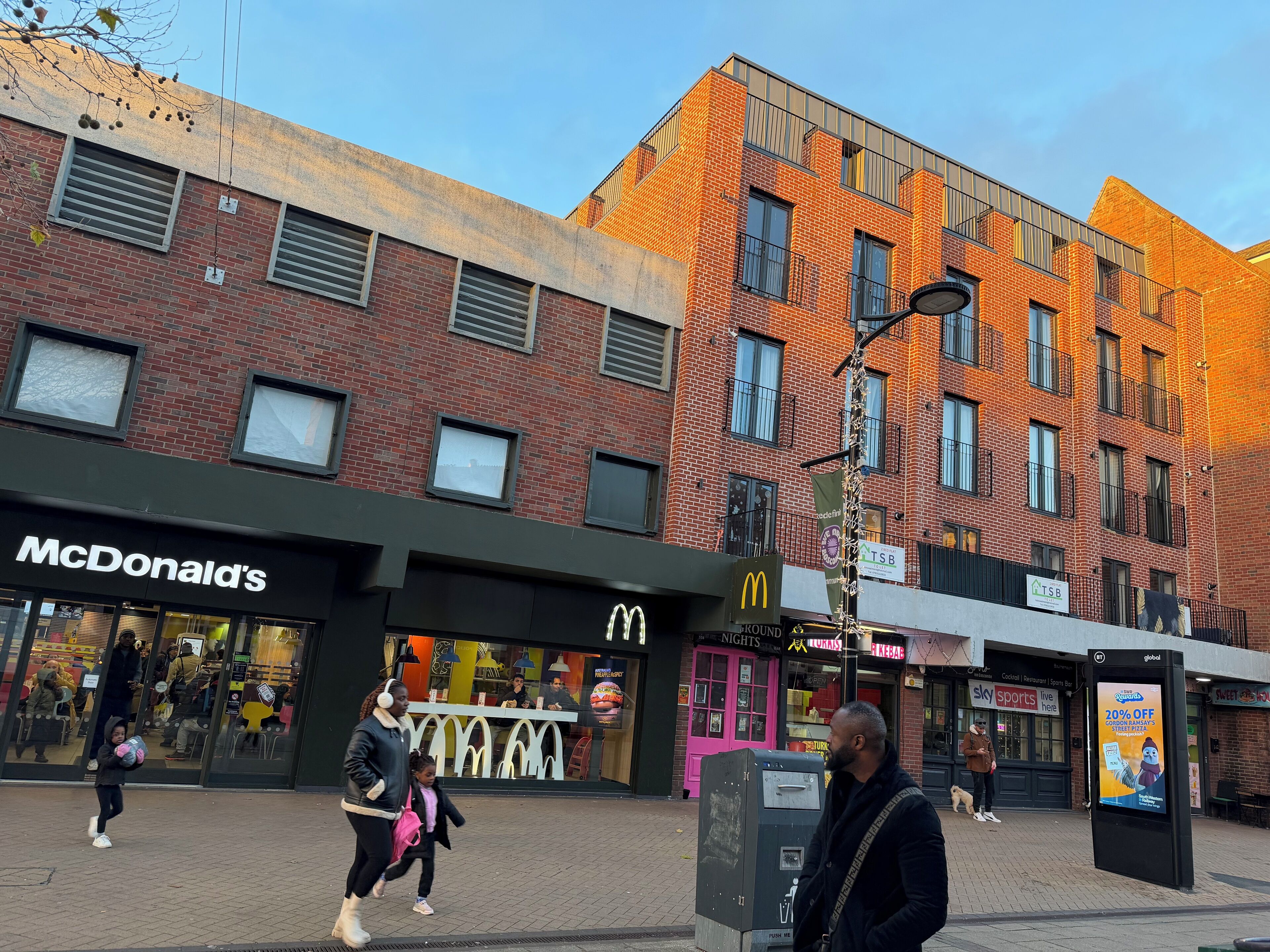 A street view with a McDonald's restaurant, a building with a brick facade, and a digital advertisement board.