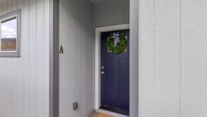 Eine dunkelblaue Tür mit einem Kranz, einem Briefkasten und einem kleinen Fenster mit Blick auf die Landschaft.