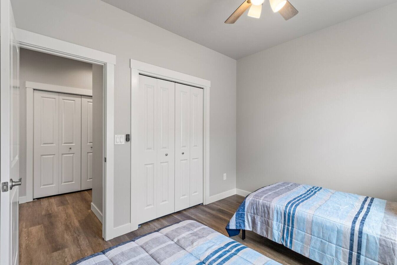 A bedroom with two beds, a ceiling fan, and a door leading to another room.