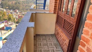 Ein schmaler Balkon mit gemustertem Bodenbelag, einem blauen Geländer und Blick auf eine Stadt.