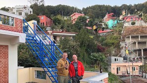 Un edificio residencial con una escalera azul, un patio con baldosas y vistas a casas coloridas al fondo.