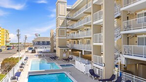 A multi-story hotel with a rooftop pool area, including lounge chairs and a swimming pool. - 1BR Oceanside Getaway: Beach, Pool & Views! (North Wildwood)