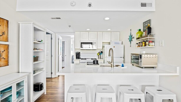 A modern kitchen with white cabinets, a central island with stools, a microwave, a refrigerator, and a toaster. - 1BR Oceanside Getaway: Beach, Pool & Views! (North Wildwood)
