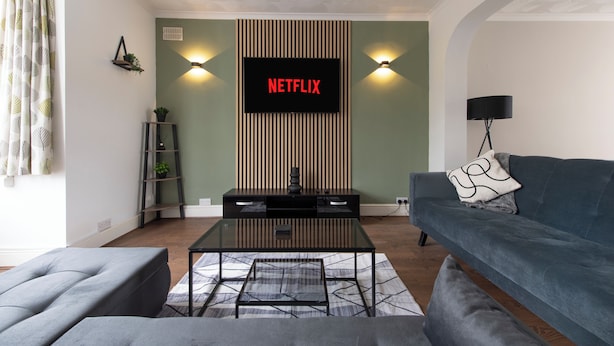 Uma sala de estar com televisão de tela plana na parede, um sofá, uma mesa de centro e um abajur.