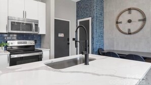 Una cocina moderna con armarios blancos, un microondas de acero inoxidable, horno empotrado, un lavamanos con grifo negro y una pared de acento azul.