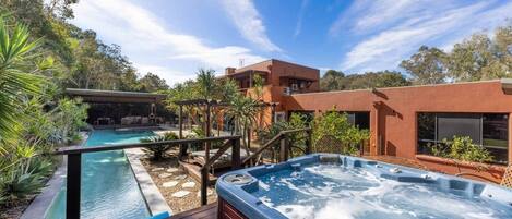 A modern outdoor pool area with a hot tub, wooden deck, and a covered seating area.