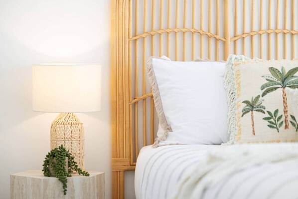 Un lit bien fait, avec un oreiller blanc et un coussin décoratif orné de motifs de palmiers.