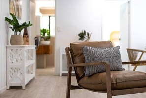 Un salon moderne avec un fauteuil en cuir marron, un coussin à motifs et une console blanche agrémentée de plantes.
