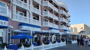 A waterfront hotel with outdoor seating, a white picket fence, and a balcony with ornate railings. - Luxury Shoal Harbor Retreat – Walk to Beach + Pool (Rehoboth Beach)