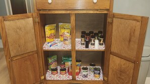 Un mueble de madera con dos puertas, que contiene diversos alimentos y condimentos.