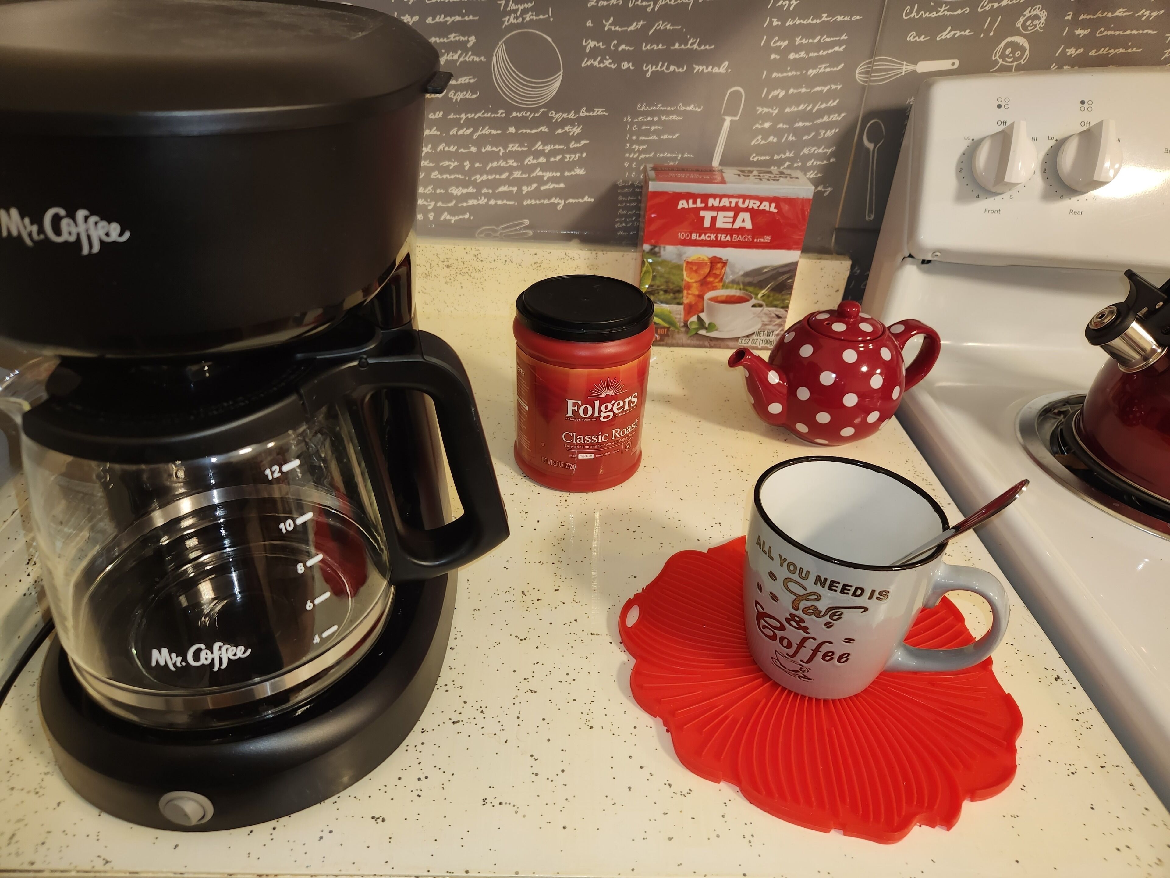 Una cocina con cafetera, taza roja, caja de té y tetera de lunares.