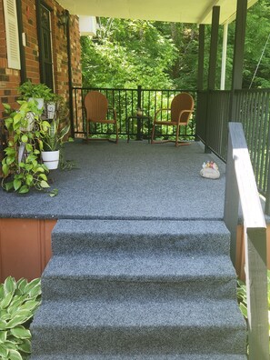 Ein überdachter Außenbereich mit einer Treppe zu einer Sitzecke, die zwei Stühle und einen kleinen Tisch umfasst.