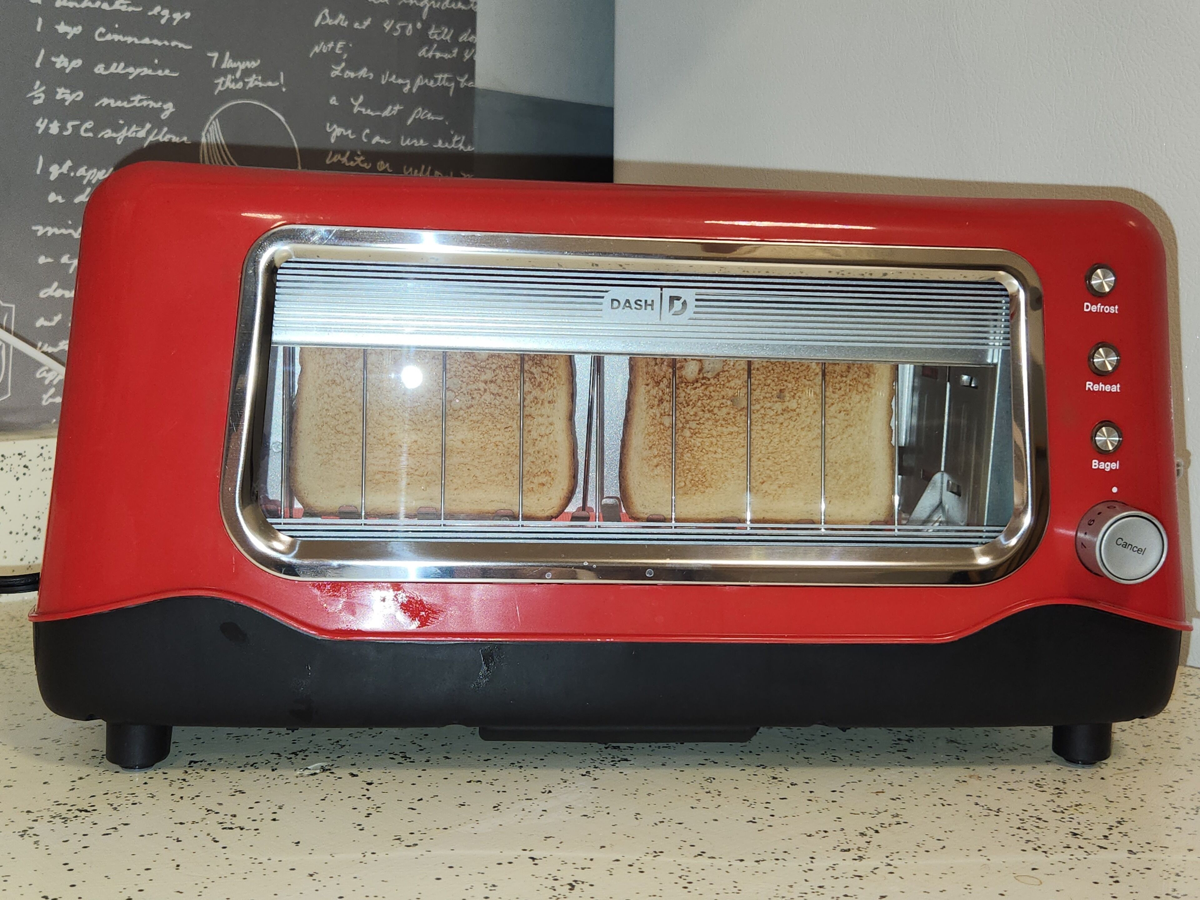 A red toaster with a transparent bread slot, a defrost button, a reheat button, and a bagel button.