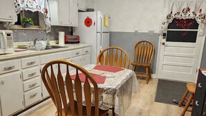 Una cocina compacta con muebles blancos, un refrigerador, un microondas y una mesa de comedor con dos sillas de madera.