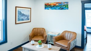 Una habitación con dos sillones de cuero marrón, una mesita de madera con una planta y un cuadro enmarcado en la pared.
