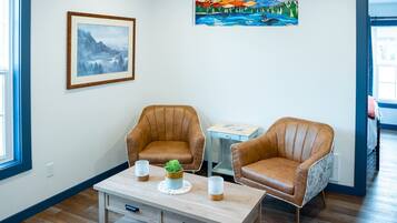 A room with two brown leather armchairs, a small wooden table with a plant, and a framed painting on the wall.