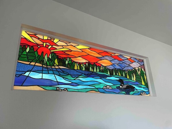 A stained glass window with a landscape scene, including a river, trees, and a mountain range. - Vasanoja Suite 102, Hyland Hotel (Palmer)