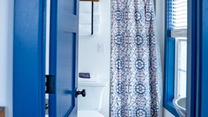 A bathroom with a toilet, a shower curtain, and a window with blinds. - Van Wormer Room 201, Hyland Hotel (Palmer)