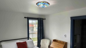 A bedroom with a bed, a chair, a desk, and a stained glass ceiling. - Bugge Room 203, Hyland Hotel (Palmer)