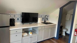 A compact kitchen with a flat-screen TV, a sink, and a refrigerator. - Snodgrass Suite 301, Hyland Hotel (Palmer)