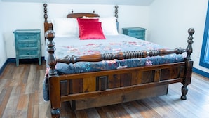 A four-poster bed with a floral bedspread and red pillows, flanked by two nightstands with drawers, in a room with wooden flooring and a window. - Snodgrass Suite 301, Hyland Hotel (Palmer)