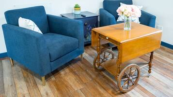 A room with a blue armchair, a wooden side table with a vase of flowers, and a blue sofa.