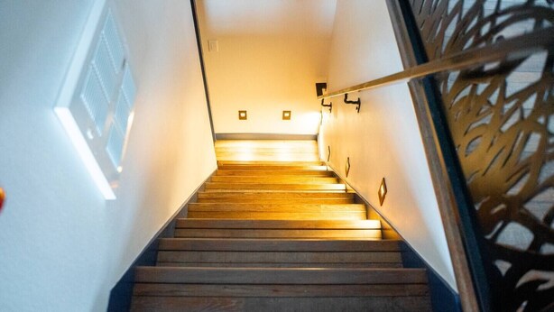 A wooden staircase with a handrail and wall-mounted light fixtures. - Snodgrass Suite 301, Hyland Hotel (Palmer)