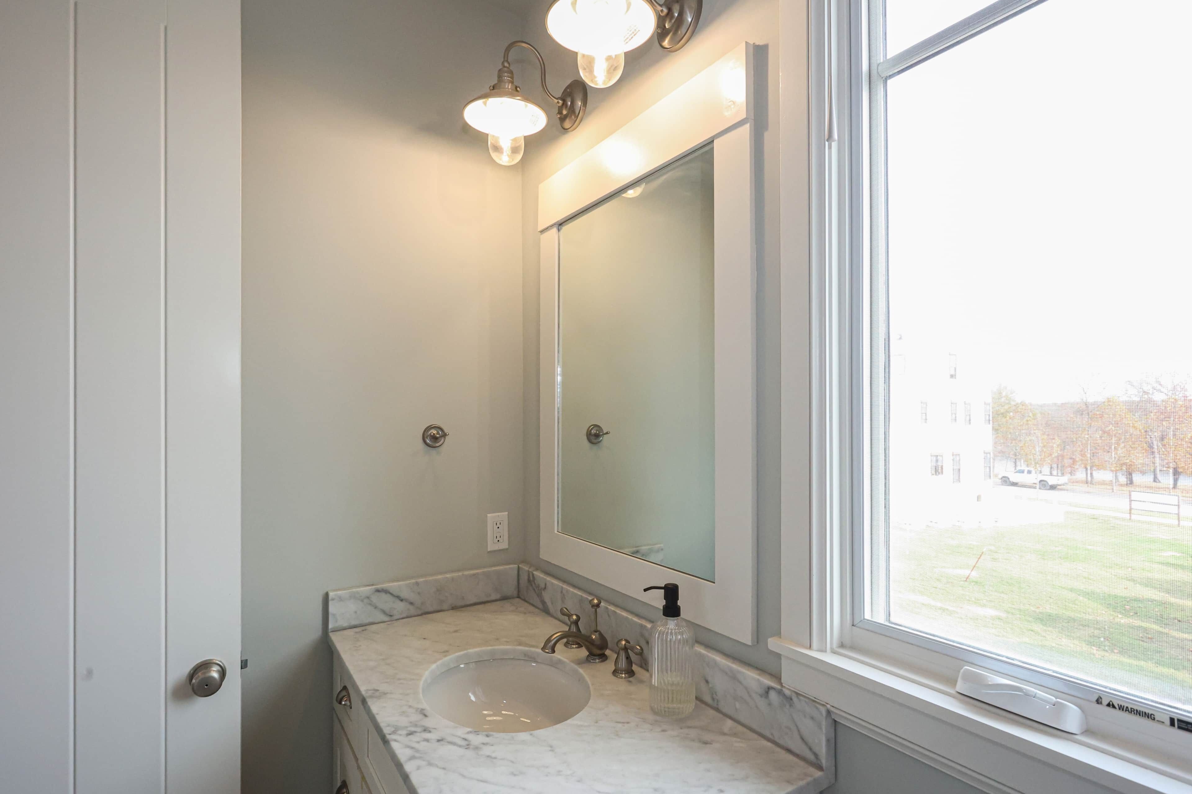 A bathroom with a marble sink, a large mirror, and a window with a view of a building and trees.