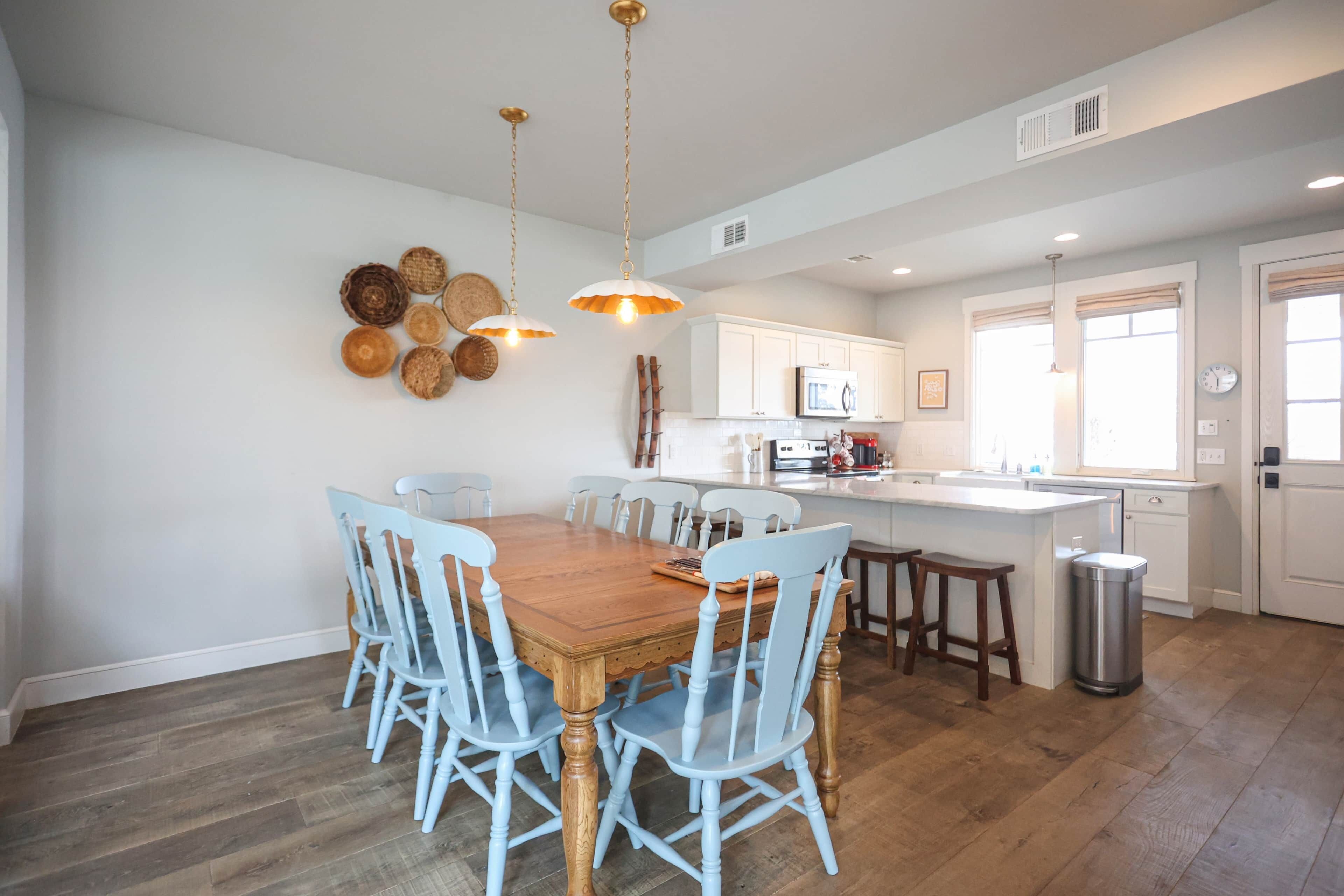 A spacious kitchen with a wooden dining table, light blue chairs, white cabinets, and a stainless steel sink.